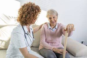 Friendly relationship between smiling caregiver in uniform and happy elderly woman. Supportive young nurse looking at senior woman. Young caring lovely care giver and happy ward