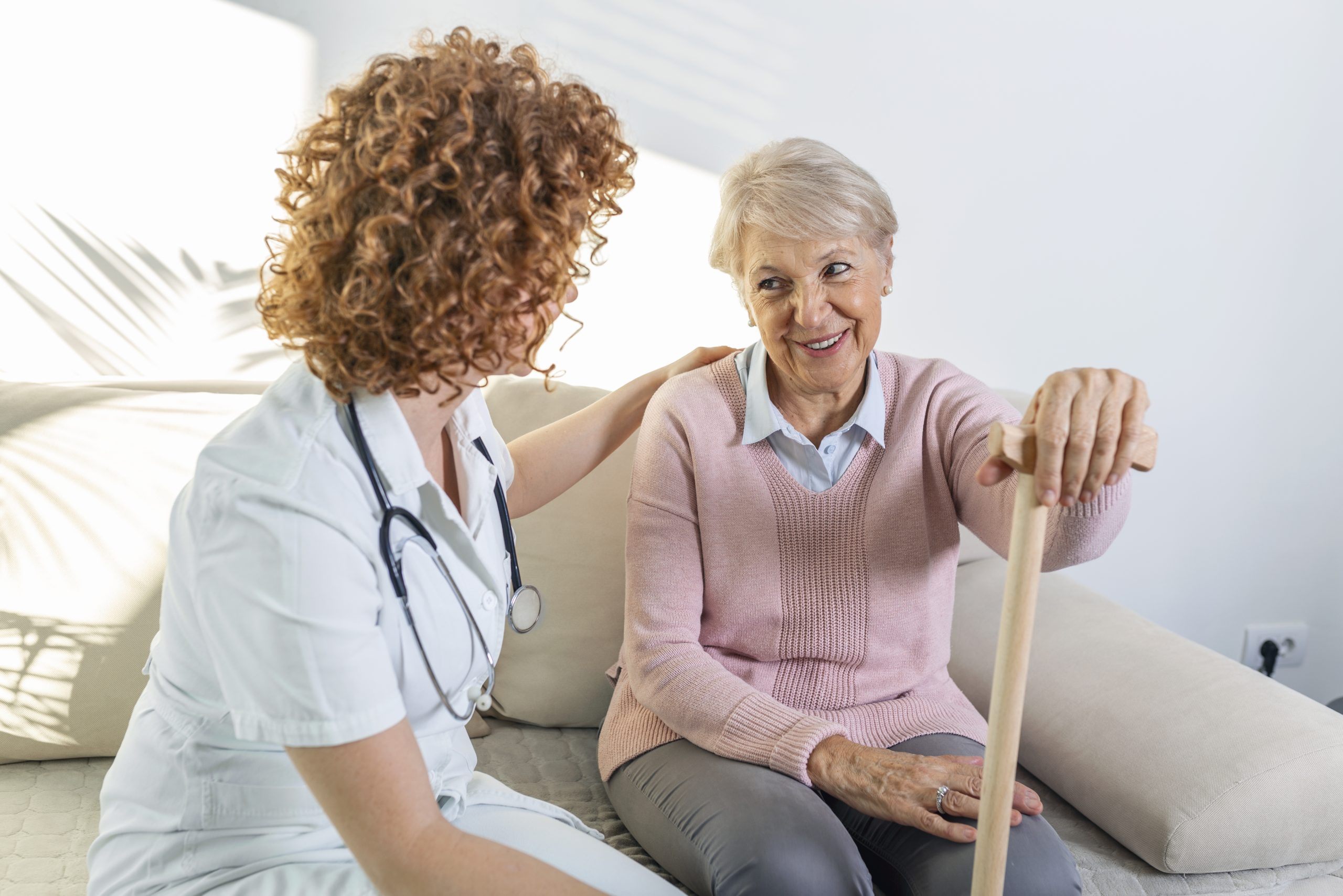 Friendly relationship between smiling caregiver in uniform and happy elderly woman. Supportive young nurse looking at senior woman. Young caring lovely care giver and happy ward